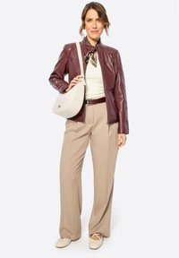 Bordeaux leren jas over een crèmekleurige top, gecombineerd met beige wijde broek en een witte handtas. Een geknoopte zijden sjaal voegt textuur toe.