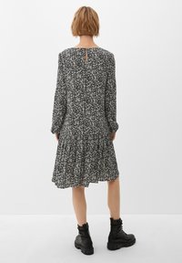 Schwarzes und weißes Blumendruckkleid mit langen Ärmeln, einem gestuften Saum und einem Schlüssellochdetail am Rücken, kombiniert mit schwarzen klobigen Stiefeln.