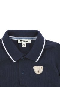 Polo shirt blu navy con colletto a righe bianche, con ricamo di un orso sul lato sinistro del petto e chiusura a due bottoni. Etichetta della taglia visibile.
