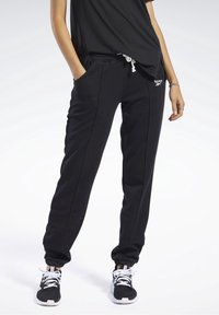 Pantalones de chándal negros hechos de tela suave, con bolsillos laterales, puños elásticos y cintura con cordón. Logo mostrado en el muslo izquierdo.