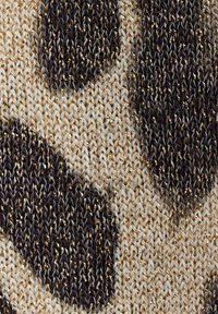Stickad textil med en krämig botten och stora abstrakta former i brunt och svart. Materialet verkar mjukt med en något strukturerad yta.