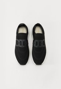 Baskets de sport noires en maille tricotée avec une texture respirante. Elles présentent une épaisse bande noire sur le dessus, une semelle blanche et un design de bout arrondi.