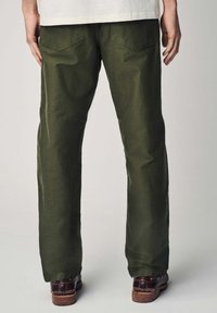 Un pantalon vert olive au design droit, avec une texture lisse, deux poches arrière et des bottes marron usées avec des coutures contrastantes.
