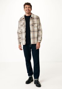 Plaid flannel shirt in beige and blue with two chest pockets, paired with black jeans and black ankle boots. Smooth texture throughout.