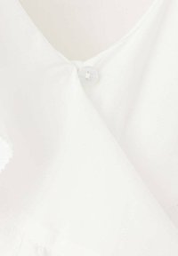 Gros plan d'un tissu blanc avec un seul bouton blanc fixant deux morceaux de tissu qui se chevauchent.