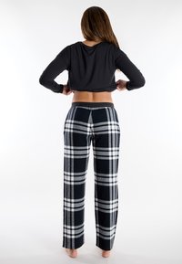 Top negro de manga larga y pantalones de pijama a cuadros en azul marino, blanco y gris. Los pantalones tienen un corte relajado y cintura elástica.