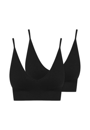 Uśmiechnięta kobieta z długimi blond włosami, ubrana w czarny bralette i czarne majtki z wysokim stanem na białym tle.