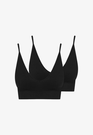 Uśmiechnięta kobieta z długimi blond włosami, ubrana w czarny bralette i czarne majtki z wysokim stanem na białym tle.