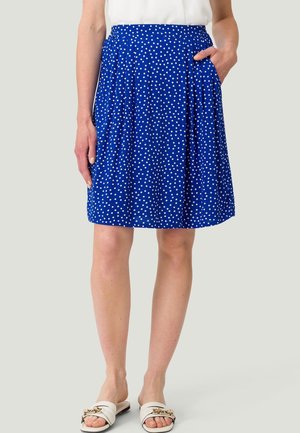 Falda azul hasta la rodilla con lunares blancos, cinturilla elástica, bolsillos laterales, combinada con top blanco y sandalias blancas sin tiras con detalle dorado.