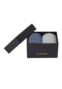 Deux pelotes de fil texturé enroulées, l'une bleu foncé et l'autre gris clair, emballées dans une boîte noire élégante avec un logo doré "MONOPRIX". Le couvercle de la boîte est partiellement ouvert.
