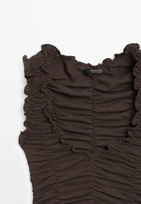 Haut sans manches marron foncé avec bords volantés et détails de tissu froncé, montrant l'étiquette Massimo Dutti au niveau de l'encolure.