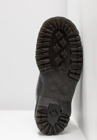 Suela de bota de goma negra con patrones de huellas profundos, formas rectangulares y de diamante. Zona de puntera reforzada y superficie texturizada para mayor agarre.