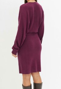 Robe en maille bordeaux à coupe décontractée, manches longues et texture côtelée. Dotée d'une ceinture mettant en valeur la silhouette.