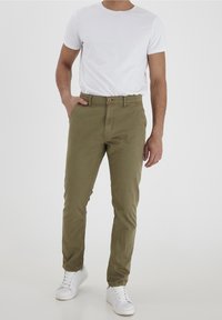 Olivově zelené bavlněné chino kalhoty s rovnými nohavicemi, předními kapsami a jedním knoflíkem na zapínání. Kombinované s bílým tričkem a teniskami.