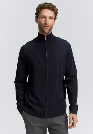 Sudadera navy de cremallera hecha de una suave tela de punto con un cuello alto. Presenta mangas largas y un cierre de cremallera suave.