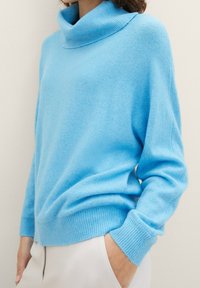 Ljusblå stickad tröja med hög, rullad krage, ribbade muddar och avslappnad passform, tillverkad av mjukt, texturerat material.