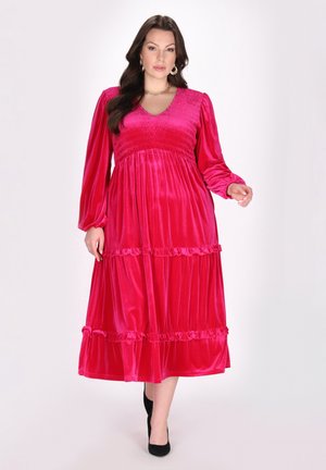 Rochie din catifea fucsia cu mâneci lungi, corset plisat, margine volan grosier și o siluetă fluidă, asortată cu pantofi cu toc înalt negri.