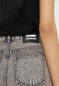 Vaqueros de mezclilla con un acabado stone-wash, que presentan una etiqueta de tela negra con el texto blanco "DRDENIM" en la parte trasera de la cintura.
