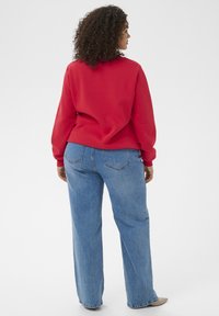 Roter Pullover mit rundem Ausschnitt und langen Ärmeln, kombiniert mit hellblauen, locker sitzenden Jeans aus Denim. Einfaches, lässiges Design ohne sichtbare Muster.