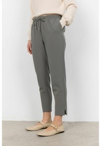 Pantaloni jogger grigi a sigaretta con vita elasticizzata, cordoncino, tasche laterali e spacco alle caviglie, abbinati a ballerine beige.