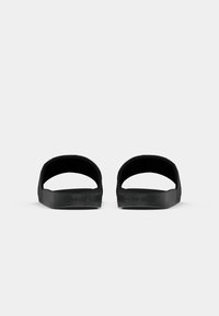 Sorte slidesandaler med en struktureret overdel, åben bag, og flad sål. Har præget branding på ydersiden. Enkel, minimalistisk design.