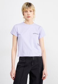 T-shirt in cotone lilla chiaro con colletto rotondo, maniche corte e un piccolo logo nero sul lato sinistro del petto. Design cropped con una vestibilità rilassata.