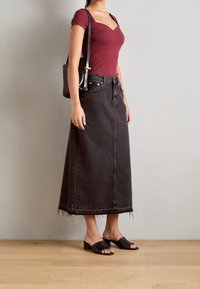 Donna che indossa un top ribbed borgogna, una gonna di denim nera a vita alta con orlo squartato, sandali neri con tacco e borsa a spalla nera.