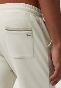 Lichtgekleurde joggers met een gestructureerde afwerking, voorzien van een achterzak accentueerd door een horizontale gestreepte bies en een klein, geborduurd hondenlogo.