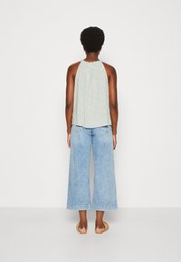 Lichtgroen mouwloos topje met een patroon, gecombineerd met lichtblauwe wijd gesneden jeans. Draagt het met platte, tan sandalen.