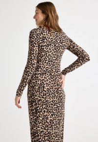 Långärmad klänning i beige med svart leopardmönster, figursydd design, mjuk textur och rund halsringning. Har en medellång silhuett.