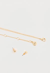 Set di gioielli in tono oro composto da una collana a catena con chiusura tipo gancio e due orecchini a perno con fondi trasparenti e accenti a piramide.