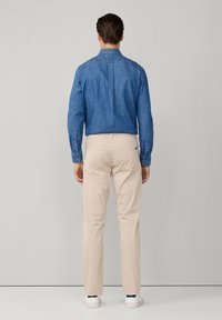 Blauwe denim overhemden met een button-down kraag en lange mouwen, gecombineerd met beige broek en witte sneakers, van achteren weergegeven.