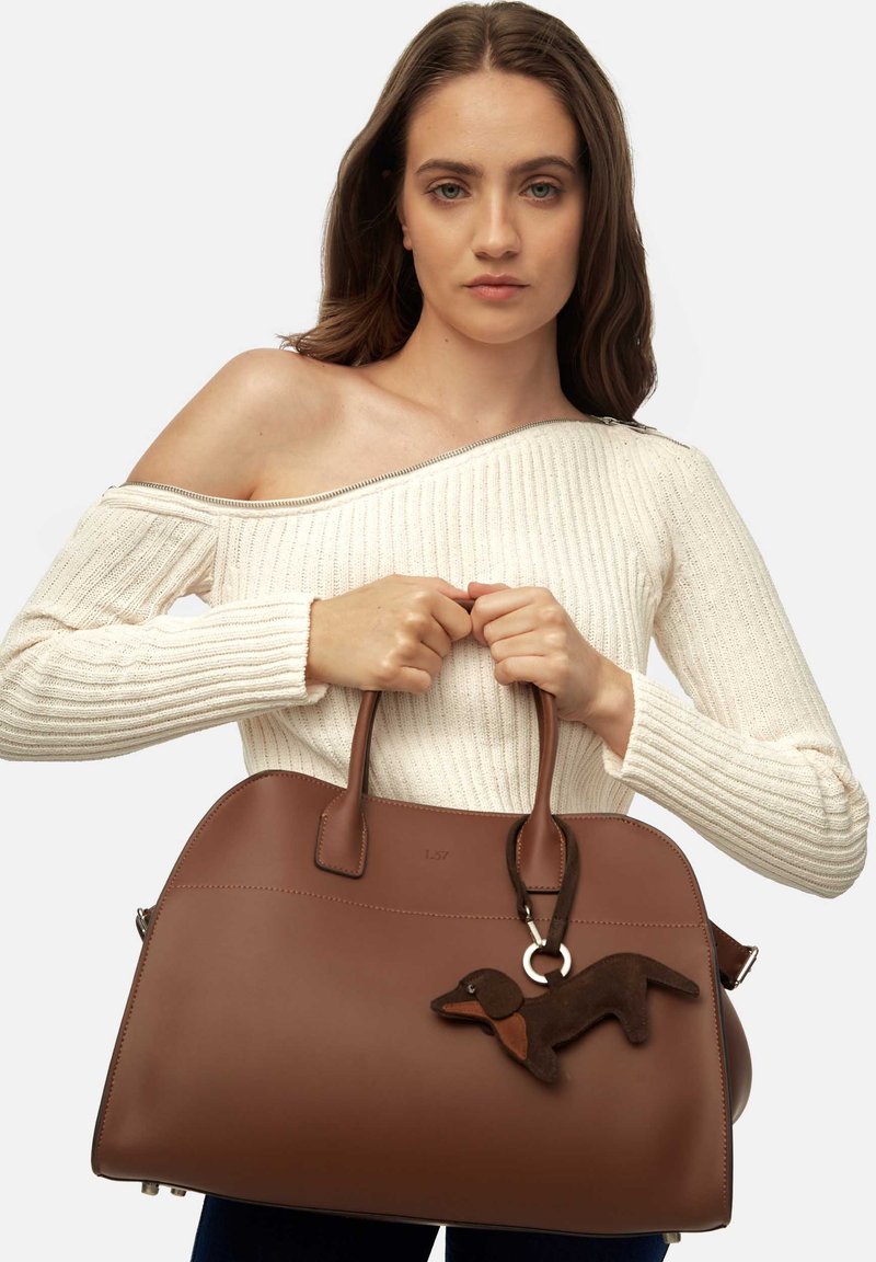 Sac à main en cuir marron de forme arrondie, avec deux poignées et un porte-clé représentant un teckel. Texture lisse avec des accents minimaux.