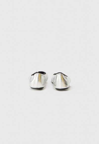 Ballerines argentées avec une finition métallique brillante, bout rond et intérieur noir doux. Détails de plis sur l'extérieur lisse. Semelle plate.