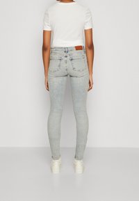 Jeans ajustados de un azul claro, fabricados en mezclilla con un acabado ligeramente desgastado. Cuentan con bolsillos traseros y un parche de cuero marrón en la cintura.