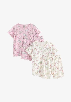 Smilende rødhåret pige iført lyserøde pyjamas med enhjørningemotiv og fluffy lyserøde enhjørningetøfler, stående og balancerende med armene strakt ud.