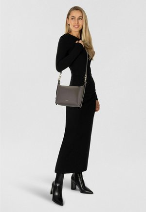 Borsa a tracolla in pelle grigia con design strutturato, ferrature argentate e tracolla regolabile. Indossata da una persona con un outfit nero aderente.