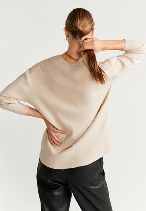 Pull en maille beige à coupe décontractée et à manches longues, doté d'une couture d'épaule légèrement tombante. Associé à un pantalon en cuir noir.