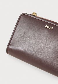 Burgundi nahast rahakott kauni disainiga, millel on kuldsed detailid ja graveeritud "BOSS". Tõmblukk servas ja tekstureeritud pind.