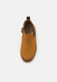 Botín de cuero marrón con una textura suave, diseño sin cordones y cremallera lateral. Tiene una lengüeta en el talón y una puntera redondeada.