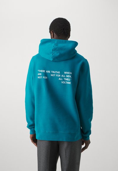 Teal sweatshirt with a hood, featuring white text on the back. The fabric appears soft and textured, with ribbed cuffs and hem.