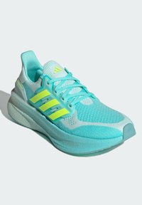 Baskets de sport bleu clair avec une tige en mesh texturé, accents jaunes contrastants et une semelle rembourrée. Caractéristiques de laçage traditionnel.