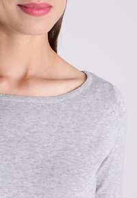 Pull gris au toucher doux, avec un col rond et des manches longues reposant sur une épaule. Gros plan mettant l'accent sur le tissu et le col.