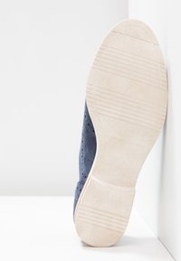 Chaussure en daim bleu marine avec détails perforés et semelle en caoutchouc blanc texturée, vue de dos, mettant en valeur son design plat.