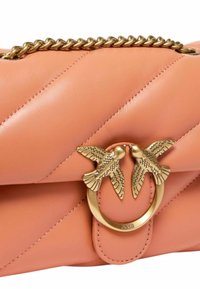 Bolso de piel melocotón con un diseño acolchado, que presenta una correa de cadena en tono dorado y un detalle de cierre en forma de pájaro en el centro.