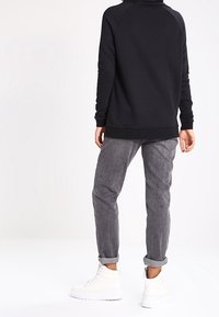 Svart polotröja med raglanärmar och ribbade muddar, parat med grå smala byxor och vita högkantiga sneakers.