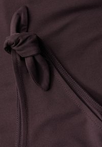 Tmavě fialová látka má uzlový detail vázání, hladký povrch a čisté švy podél okrajů. Jednoduchý a minimalistický design.