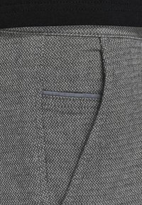 Tissu texturé gris avec un motif subtil, présentant une poche étroite avec une bordure sombre contrastante et une taille lisse au-dessus.