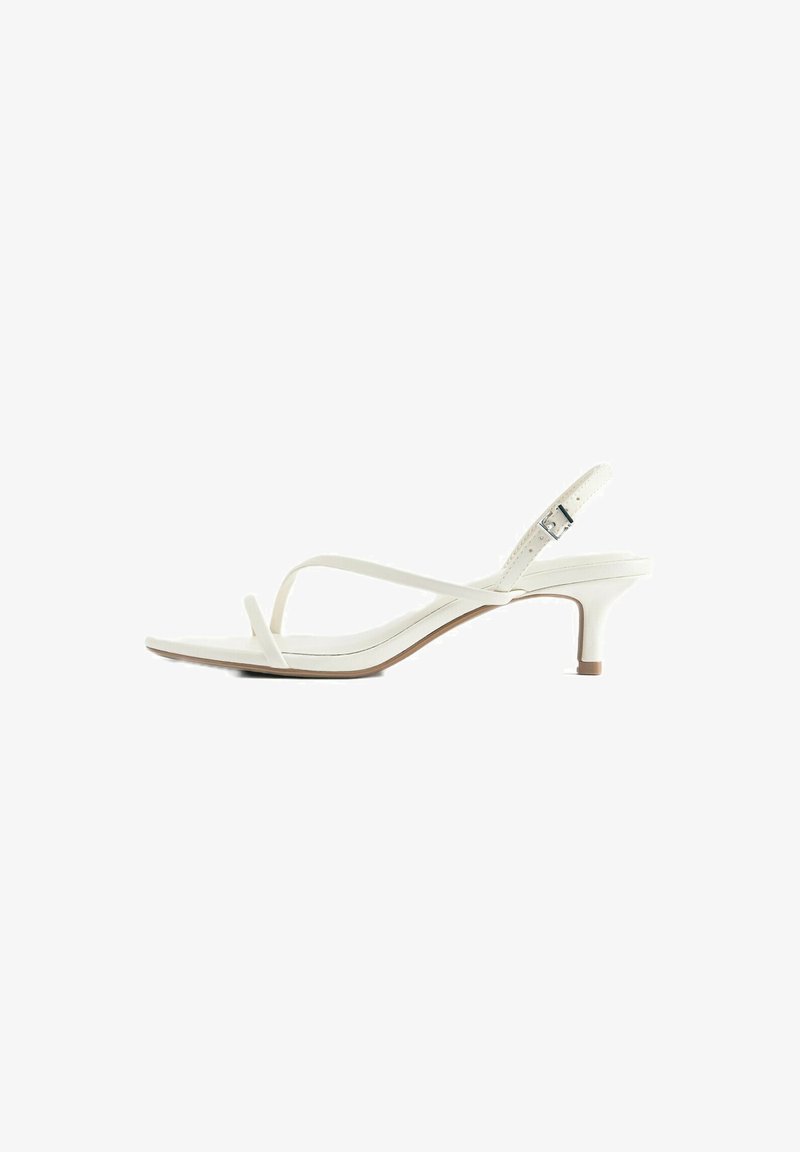 Sandale blanche à brides fines, bout ouvert, talon fin, boucle d’orteil et bride de cheville réglable avec boucle argentée.