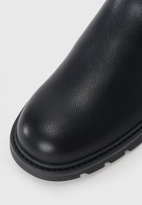 Zwarte neplederen boot met een gladde afwerking, ronde neus en een gestructureerde rubberen zool. Zichtbare stiksels benadrukken de basis.